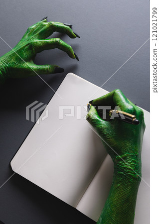 Vertical image of green monster hands writing notebook with copy space on grey background 121021799