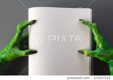Green monster hands holding notebook with copy space on grey background 121021818