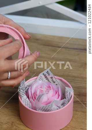 A woman is wrapping a flower-shaped candle in a gift box. Close-up. 121022484
