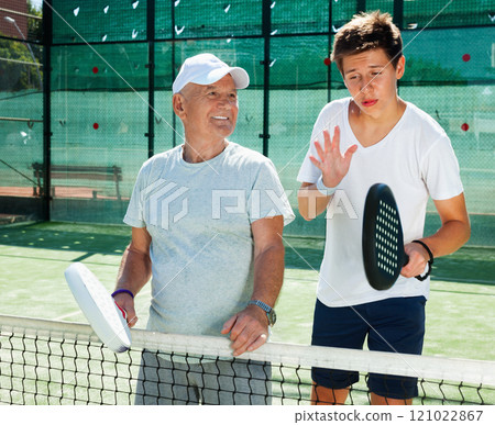 Padel players of different generations talking on court playing paddle Padel players of different generations talking on court playing paddle 121022867