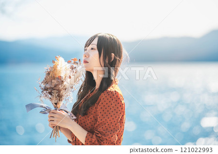 A woman in a red dress standing by a lake with dried flowers A woman in a red dress standing by a lake with dried flowers 121022993
