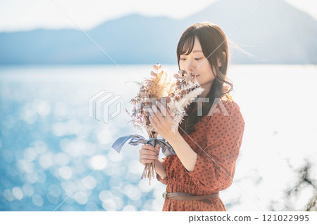 一個穿紅裙子的女人站在湖邊，手裡拿著乾燥花 121022995