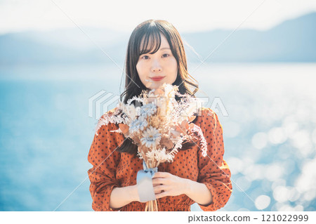 A woman in a red dress standing by a lake with dried flowers 121022999