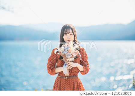 A woman in a red dress standing by a lake with dried flowers 121023005