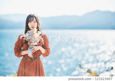 A woman in a red dress standing by a lake with dried flowers 121023007