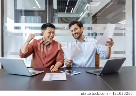 Business colleagues celebrate success with laptops and documents. Smiling coworkers review project results on paper and phone, highlighting teamwork and achievement in modern office. Business colleagues celebrate success with laptops and documents. Smiling coworkers review project results on paper and phone, highlighting teamwork and achievement in modern office. 121023293