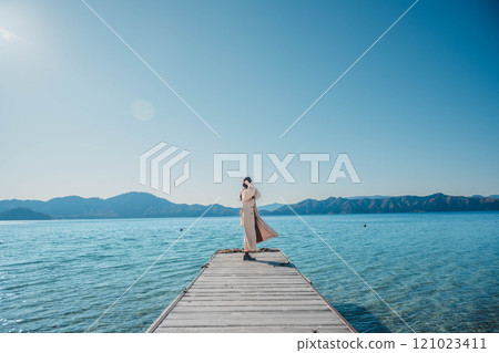 Young woman standing by a lake under a blue sky Young woman standing by a lake under a blue sky 121023411