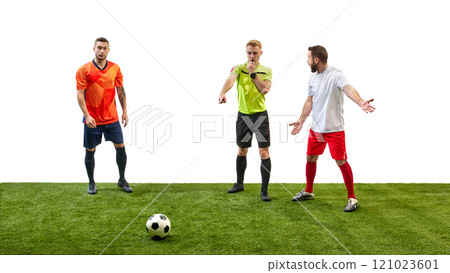 Soccer referee blowing a whistle and making gesture to signal foul while player prepares to take penalty, highlighting rule enforcement in game. 121023601
