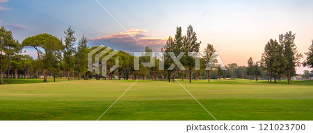 A tranquil golf course with lush greenery and a peaceful tree line, illuminated by the gentle hues of a serene sunset sky. 121023700