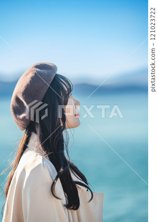 A young woman wearing a beret and a trench coat with a blue sky in the background 121023722