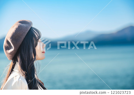 藍天下戴著貝雷帽和風衣的年輕女子 121023723
