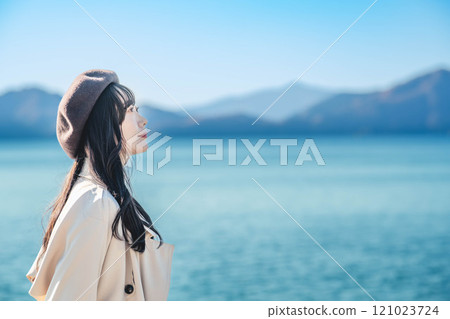 藍天下戴著貝雷帽和風衣的年輕女子 121023724