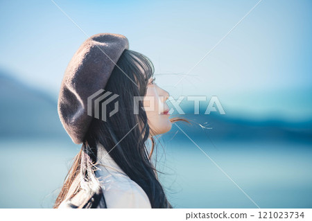 A young woman wearing a beret and a trench coat with a blue sky in the background A young woman wearing a beret and a trench coat with a blue sky in the background 121023734