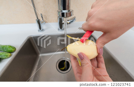 Peeling a fresh pear under running water with waste directed into a garbage disposer. Peeling a fresh pear under running water with waste directed into a garbage disposer. 121023741