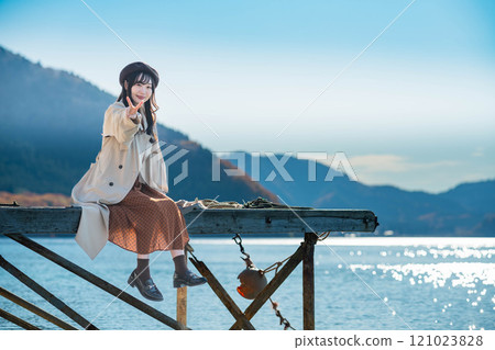 坐在湖邊的貝雷帽和風衣的年輕女子 121023828