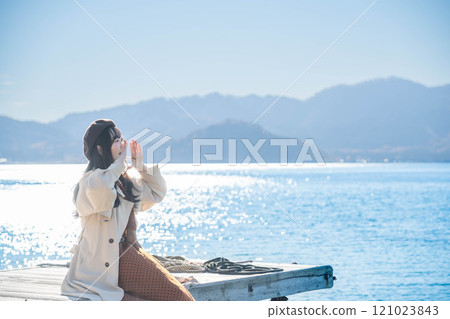 坐在湖邊的貝雷帽和風衣的年輕女子 121023843