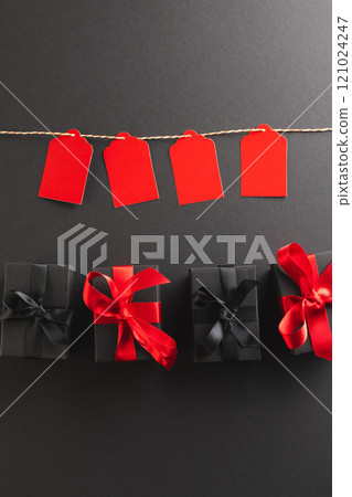 Vertical image of red gift tags on pegs and black gift boxes with copy space over black background Vertical image of red gift tags on pegs and black gift boxes with copy space over black background 121024247