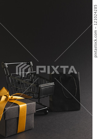 Vertical image of gift box with ribbon, gift bag, shopping trolley, copy space over black background 121024285