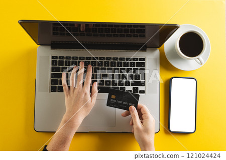Caucasian woman with credit card using laptop and smartphone with copy space on yellow background 121024424