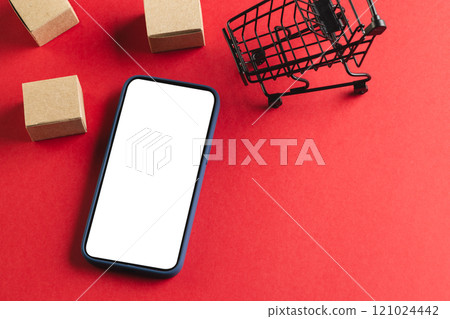Smartphone with copy space and trolley with boxes on red background Smartphone with copy space and trolley with boxes on red background 121024442
