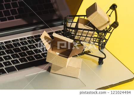 Laptop with copy space and trolley with boxes on yellow background 121024494
