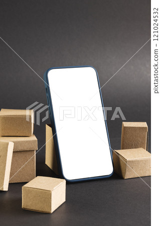 Vertical image of smartphone with blank screen and cardboard boxes, copy space on black background 121024532