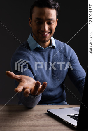 Vertical image of biracial businessman pointing and with laptop and copy space on black background Vertical image of biracial businessman pointing and with laptop and copy space on black background 121024577