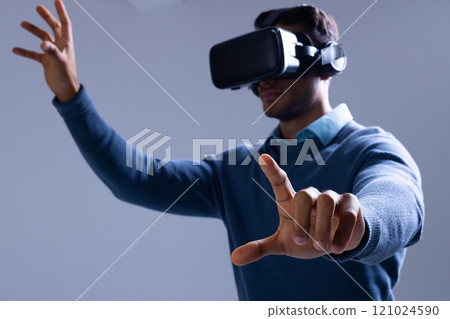 Biracial businessman using vr headset and pointing with fingers on grey background Biracial businessman using vr headset and pointing with fingers on grey background 121024590