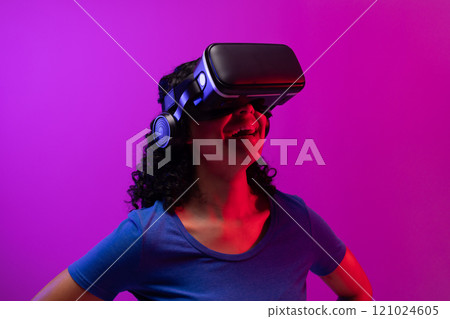 Biracial woman using vr headset on neon pink to purple background Biracial woman using vr headset on neon pink to purple background 121024605