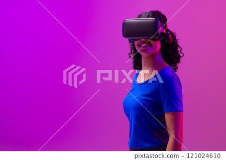 Biracial woman using vr headset on neon pink to purple background Biracial woman using vr headset on neon pink to purple background 121024610