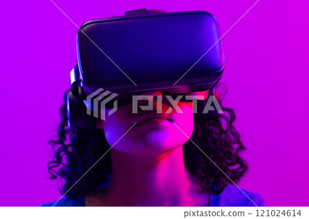 Biracial woman using vr headset on neon pink to purple background Biracial woman using vr headset on neon pink to purple background 121024614