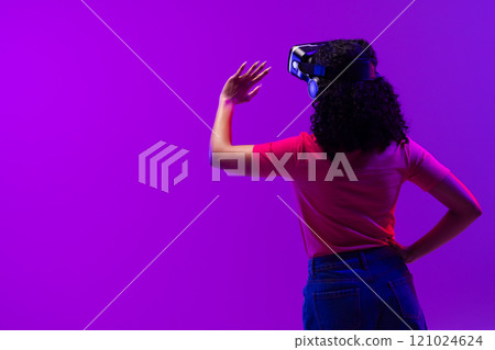 Biracial woman using vr headset and pointing on neon pink to purple background Biracial woman using vr headset and pointing on neon pink to purple background 121024624