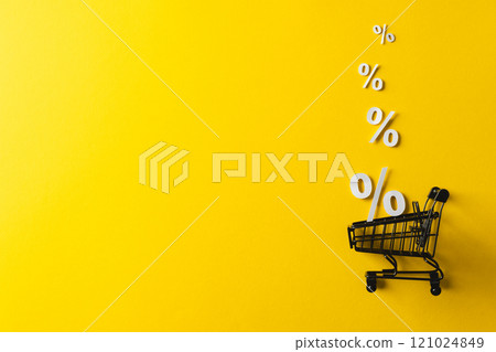 Shopping trolley and white percent signs with copy space on yellow background 121024849
