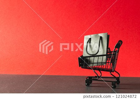 Black gift bag in shopping trolley with copy space on red background Black gift bag in shopping trolley with copy space on red background 121024872