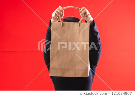 Caucasian woman holding paper shopping bag with copy space on red background 121024907