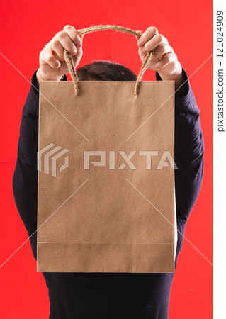 Caucasian woman holding paper shopping bag with copy space on red background Caucasian woman holding paper shopping bag with copy space on red background 121024909