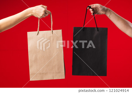 Hands of caucasian women holding black and brown gift bags with copy space on red background Hands of caucasian women holding black and brown gift bags with copy space on red background 121024914