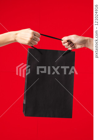 Hands of caucasian women holding black gift bag with copy space on red background Hands of caucasian women holding black gift bag with copy space on red background 121024916