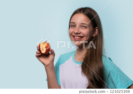 Young girl smiles brightly, holding an apple 121025309