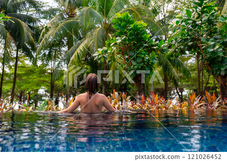 Enjoy a delightful experience of relaxing in a tropical pool surrounded by swaying palm trees 121026452