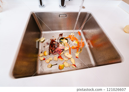 Food waste and vegetable scraps in a kitchen sink with running water and disposer. Food waste and vegetable scraps in a kitchen sink with running water and disposer. 121026607