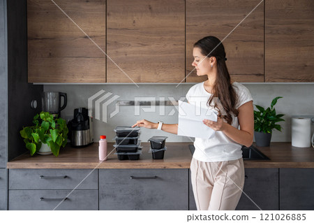 Young woman with healthy diet plan for weight loss, delivery of daily ready meal menu. Food ordered with mobile phone app. Balanced portion with dish. Pre-cooking. Young woman with healthy diet plan for weight loss, delivery of daily ready meal menu. Food ordered with mobile phone app. Balanced portion with dish. Pre-cooking. 121026885