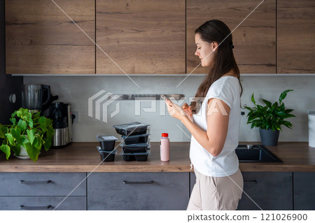 Young woman with healthy diet plan for weight loss, delivery of daily ready meal menu. Woman using meal tracker app on phone. Balanced portion with dish. Pre-cooking. 121026900