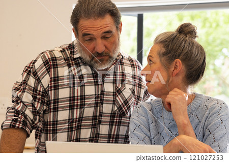 Mature couple discussing plans at home, looking at laptop screen together 121027253