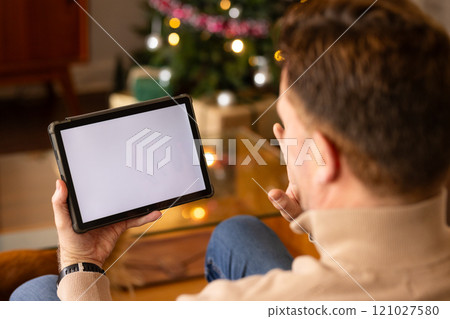 senior man video chatting on tablet by Christmas tree at home, copy space 121027580