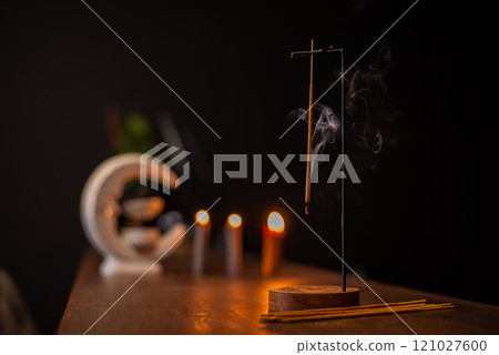 incense stick smokes on a wooden stand on a dark background. Aromatherapy, Smoke while burning incense. smoke for prayers and meditation. prayer to buddha. incense for relaxation and yoga incense stick smokes on a wooden stand on a dark background. Aromatherapy, Smoke while burning incense. smoke for prayers and meditation. prayer to buddha. incense for relaxation and yoga 121027600
