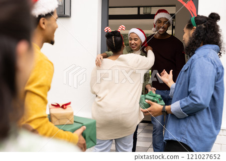 Christmas time, young multiracial friends exchanging gifts and hugs at doorstep 121027652