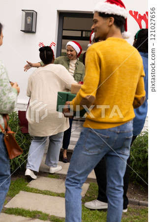 Christmas time, multiracial friends arriving at party, exchanging gifts and warm hugs at doorstep 121027656