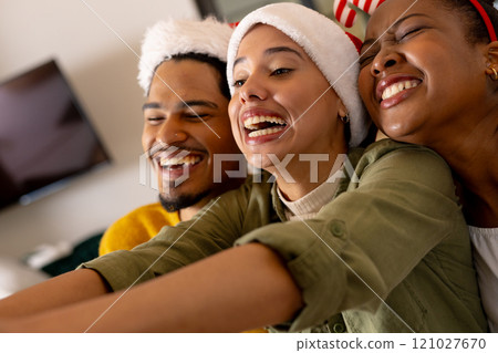 Young multiracial friends wearing Santa hats laughing and taking selfie at Christmas party, at home Young multiracial friends wearing Santa hats laughing and taking selfie at Christmas party, at home 121027670