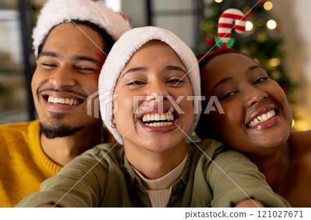 Taking selfie, young multiracial friends wearing santa hats smiling at christmas, at home 121027671